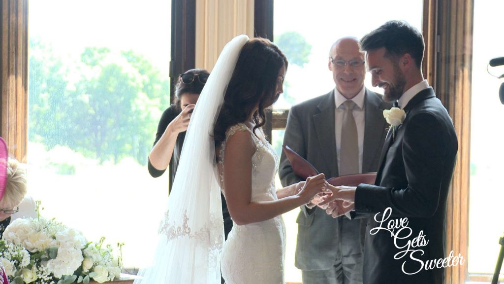 the bride and groom smile as they exchange wedding rings on the wedding video in front of the huge windows overlooking the lake at Armathwaite hall Hotel in Keswick Cumbria
