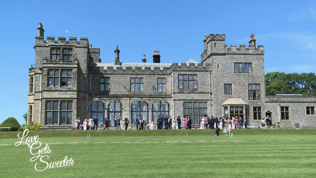 a wide shot of the stunning countryside lake district venue armathwaite hall with the wedding guests outside on the lawn